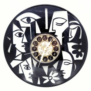 May include: A black vinyl record clock featuring white cut-out abstract faces and floral designs. The clock face in the center has gold-colored numerals and hands. A unique, artistic wall clock.