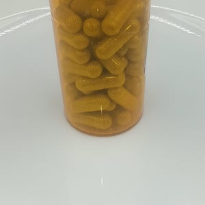 May include: A clear amber prescription bottle filled with yellow capsules. The white cap has the words "push down" printed on it. The bottle is sitting on a white surface.