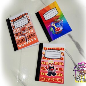 May include: Three composition notebooks with different Inside Out characters. The first notebook features a red and orange background with the word "Anxiety" repeated in a pattern. The second notebook features a rainbow background with the characters Joy, Sadness, Fear, Disgust, and Anger. The third notebook features a red and orange background with the word "Anger" repeated in a pattern.