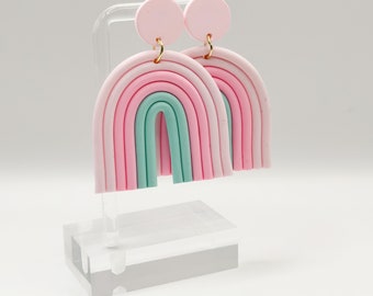 Könnte beinhalten: Ein Paar Regenbogen-Ohrringe zum Hängen. Die Ohrringe sind aus Polymer Clay gefertigt und haben ein mehrfarbiges Regenbogen-Design in den Farben Rosa, Hellrosa und Grün.