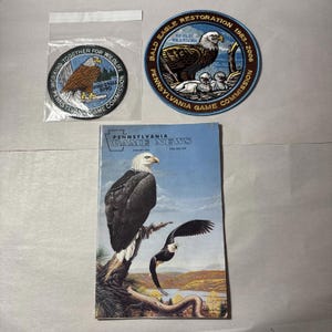May include: An assortment of items featuring bald eagles. Includes a magazine titled "Pennsylvania Game News" with an eagle illustration, and two patches with eagle designs and text related to wildlife conservation.