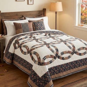 May include: A bedding set featuring a double wedding ring quilt pattern in cream, navy blue, and tan. The quilt includes floral and plaid fabric patches, complemented by matching pillow shams with similar patterns, all arranged on a wooden bed frame.