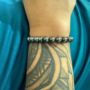 May include: A black beaded bracelet with a silver metal bead accent. The bracelet is worn on a person's wrist.