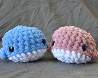 Könnte beinhalten: Zwei gehäkelte Wal-Plüschtiere, eines blau und eines rosa, mit weißen gehäkelten Bäuchen und schwarzen Augen.