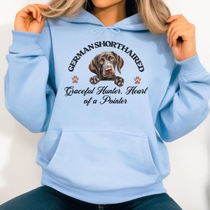 May include: Light blue hoodie with a front pocket and a graphic of a German Shorthaired Pointer. The graphic includes the text "GERMAN SHORTHAIRED" above the dog image and "Graceful Hunter, Heart of a Pointer" below.