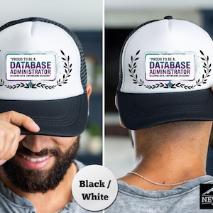 May include: Black and white trucker hat with the text "PROUD TO BE A DATABASE ADMINISTRATOR". The hat has a white front panel, a black brim, and a black mesh back. The text is in a rectangular frame with laurel leaves.