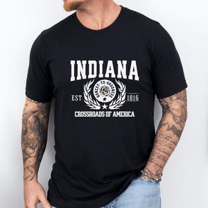 May include: Black t-shirt with the word "INDIANA" in large white block letters. Below the word "INDIANA" is the text "EST 1816" and "CROSSROADS OF AMERICA". The shirt has a crew neck and short sleeves.
