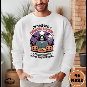 May include: A white crewneck sweatshirt featuring a graphic of a skeleton wearing glasses and a cape, reading a book. The design includes two jack-o'-lanterns, bats, and the text: I'M PROUD TO BE A FINANCIAL ADVISOR... BECAUSE EVEN GHOSTS NEED TO SAVE THEIR BOOKS!