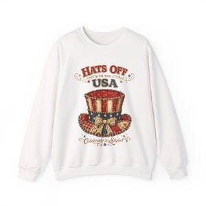 May include: White sweatshirt with a patriotic design. The graphic features a top hat in red, white, and blue, and the text "Hats Off to the USA" and "Celebrate in Style!"