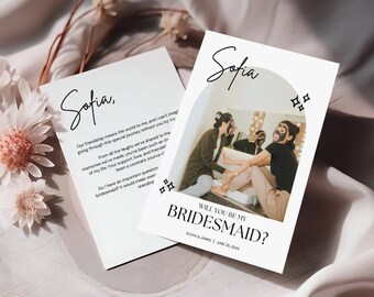 May include: A white card with a photo of two people wearing face masks. The text on the card reads "Sofia, Will you be my Bridesmaid?" with the date "June 25, 2023".