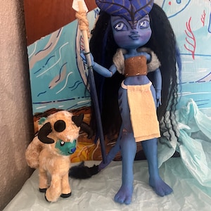 May include: A blue-skinned doll with long black hair and a brown and beige outfit holds a spear. The doll is standing next to a small, fluffy, tan and blue animal with horns.