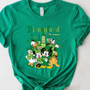 May include: Green t-shirt featuring a graphic of Disneyland characters dressed for St. Patrick's Day. The design includes Mickey Mouse, Donald Duck, Goofy, and Minnie Mouse, with the Disneyland logo.
