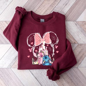Peut inclure: Sweat-shirt bordeaux avec un motif d'un n&oelig;ud rose, d'un ch&acirc;teau et de deux personnages de dessins anim&eacute;s. Le motif comprend des c&oelig;urs et des feux d'artifice. Le sweat-shirt est en mati&egrave;re douce, adapt&eacute; au port d&eacute;contract&eacute;.