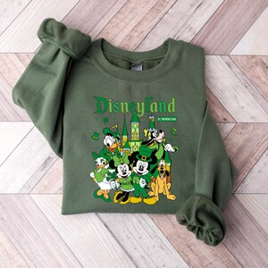May include: Green sweatshirt with the word "Disneyland" in a decorative font, along with "St. Patrick's Day". The graphic features Disney characters dressed in green, including Mickey Mouse, Donald Duck, and Pluto.