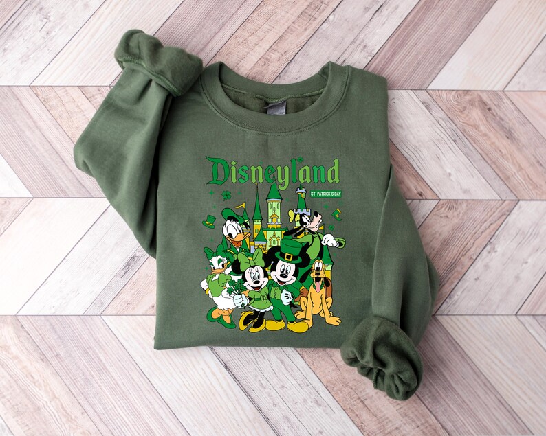 May include: Green sweatshirt with the word "Disneyland" in a decorative font, along with "St. Patrick's Day". The graphic features Disney characters dressed in green, including Mickey Mouse, Donald Duck, and Pluto.