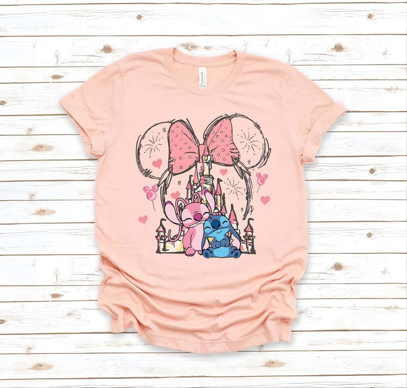 Peut inclure: T-shirt rose clair avec un motif de ch&acirc;teau, deux personnages de dessins anim&eacute;s et un grand n&oelig;ud. Les personnages sont roses et bleus. Le t-shirt a un col rond et des manches courtes.