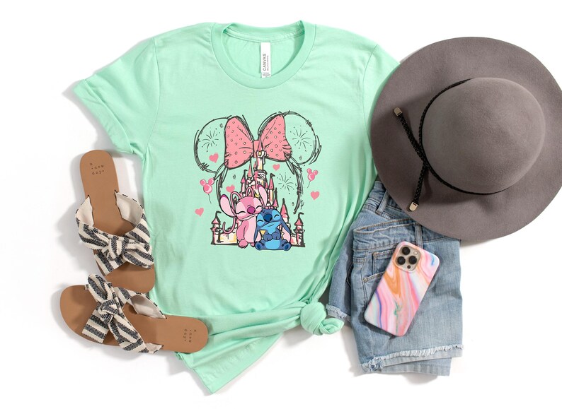 Peut inclure: Un t-shirt vert menthe avec un motif des personnages Disney Stitch et Angel, un n&oelig;ud rose et un ch&acirc;teau. Le t-shirt est pr&eacute;sent&eacute; avec des sandales, un short en jean, un chapeau gris et une coque de t&eacute;l&eacute;phone.