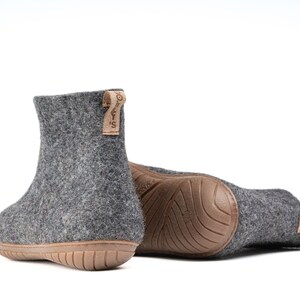 A pair of gray felt slippers with a brown rubber sole. The slippers have a brown leather tag with the text "WOOLLY'S" on them.