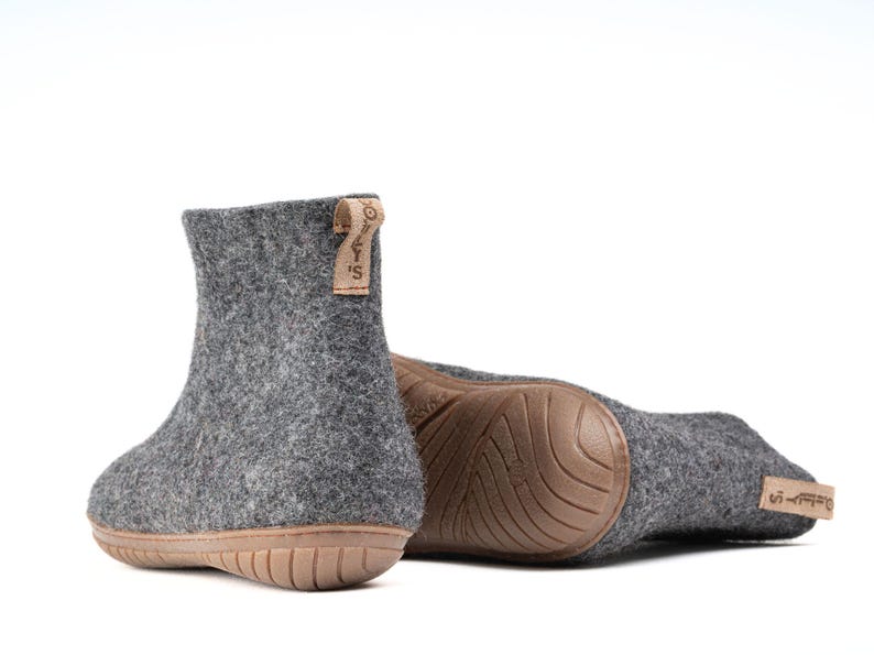 A pair of gray felt slippers with a brown rubber sole. The slippers have a brown leather tag with the text "WOOLLY'S" on them.