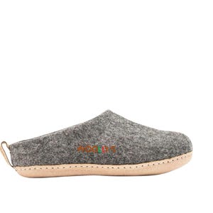 May include: Gray felt slipper with a light-colored sole and a small leather loop on the heel. The word "WOOLIES" is embroidered in colorful letters on the side. The slipper is designed for indoor wear.