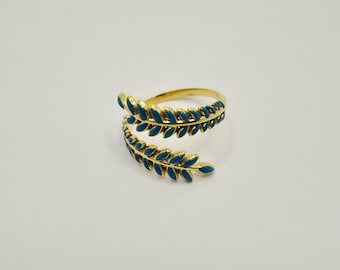 Könnte beinhalten: Ein goldfarbener Ring mit einem Blattdesign. Die Blätter sind teal und umschlingen den Finger. Der Ring befindet sich auf einem weißen Hintergrund.