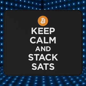 May include: Black rectangular mousepad with the text "KEEP CALM AND STACK SATS" in white. A Bitcoin symbol is at the top. The mousepad is against a blue background with small, evenly spaced, blue lights.