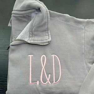 May include: A gray zip-up sweatshirt with a pink embroidered monogram "L&D" on the front.