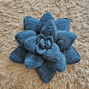 May include: A blue crocheted flower-shaped cushion. The cushion is made of a soft, fuzzy material and has a textured surface.