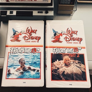 May include: Two VHS tapes of the horror film "Friday the 13th" on a white background. The first tape is the original "Friday the 13th" and the second tape is "Friday the 13th Part 2". Both tapes feature the Walt Disney Home Video logo with Mickey Mouse dressed as a wizard.