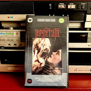May include: A VHS tape featuring a black and white image of a vampire and a woman on the cover. The title of the film is "Nosferatu" and the tape is labelled "Warner Home Video".