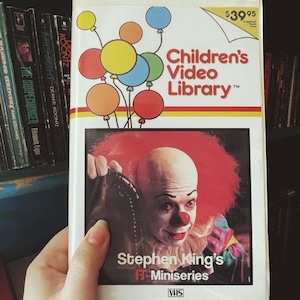 May include: A VHS tape from the Children's Video Library series. The tape features a colorful illustration of balloons and the text "Children's Video Library." Below, the cover art for Stephen King's IT Miniseries shows a clown with red hair and makeup.