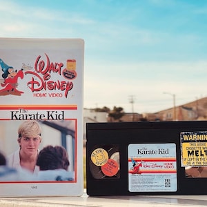 May include: Two VHS tapes, one with a blue and white label featuring the Walt Disney Home Video logo and the title "The Karate Kid", and the other with a black label featuring the title "The Karate Kid" and a warning that the cassette will melt if left in the car or in the sun.