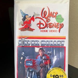 Könnte beinhalten: Ein VHS-Kassetten-Etui mit einem gelben Aufkleber, auf dem "Previously Viewed 19,95 € Fully Guaranteed" steht. Das Etui zeigt ein Cartoon-Bild von Mickey Mouse, der als Zauberer verkleidet ist. Der Titel des Films ist "Silver Bullet" und das Logo von Walt Disney Home Video befindet sich oben rechts. Das Etui ist weiß mit roten und gelben Akzenten.