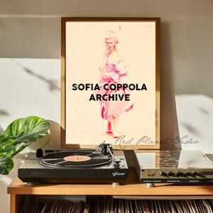 May include: A framed print with a pink and white illustration of a woman in a dress and a wig. The text "SOFIA COPPOLA ARCHIVE" is printed in black at the bottom of the print.