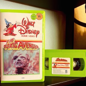 May include: A VHS tape of the movie "The Toxic Avenger" with a green case and a label featuring a cartoon image of a monster. The label also includes the text "Walt Disney Home Video" and a restricted rating symbol.