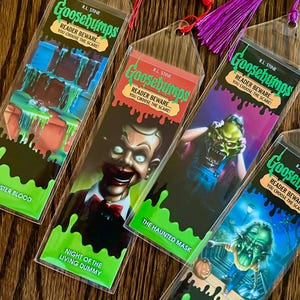 May include: Four Goosebumps book bookmarks with green, red, purple, and blue tassels. The bookmarks feature covers from the books "Night of the Living Dummy", "The Haunted Mask", "The Haunted Mask II", and "Monster Blood".
