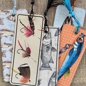 May include: Five different bookmarks featuring fishing-themed illustrations. The bookmarks are made of paper and have a tassel attached to the top. The illustrations include a variety of fish, fishing lures, and fishing flies.