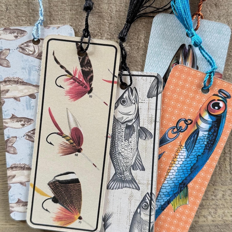 May include: Five different bookmarks featuring fishing-themed illustrations. The bookmarks are made of paper and have a tassel attached to the top. The illustrations include a variety of fish, fishing lures, and fishing flies.