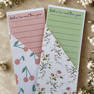 May include: Two decorative bookmarks. One has a pink background with cherries and the text "Books I've read this year." The other has a green background with floral patterns and the same text. Both have lined pages.