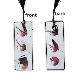 May include: A bookmark with a black tassel features illustrations of different types of fishing flies on both sides. The front side shows four flies with numbers 66, 68, 69, and 70. The back side shows three flies with numbers 67, 69, and 71.