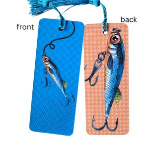May include: A double-sided bookmark with a blue and orange background. The front features a blue and silver fish lure with a blue and silver fish on a blue background. The back features a blue and silver fish lure with a blue and silver fish on an orange background. The bookmark has a blue tassel.