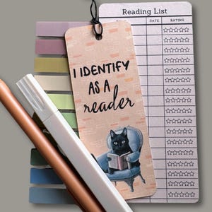 May include: A bookmark with the text "I Identify as a reader" and a black cat reading a book. A "Reading List" notepad and colorful sticky notes are also visible. Two pens and a white highlighter are in the image.