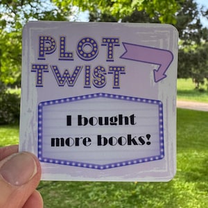 May include: A square sticker with the words "PLOT TWIST" in purple letters with a marquee-style border. Below, it reads "I bought more books!" in a similar style. The background is a light purple with a lavender arrow.