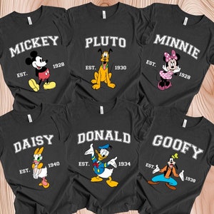 May include: Six black t-shirts with different Disney characters printed on them. Each shirt has the character's name and the year they were established. The characters are Mickey Mouse, Pluto, Minnie Mouse, Daisy Duck, Donald Duck, and Goofy.