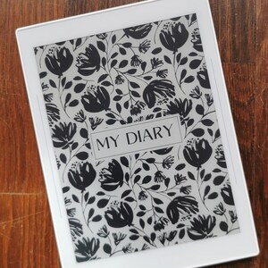以下が含まれることがあります： 画面に白黒の花柄が描かれた白い電子書籍リーダー。画面には「MY DIARY」という文字が表示されています。
