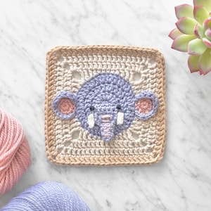 May include: A crocheted square with an elephant face design. The elephant is purple with pink ears and white tusks. The square is beige with a brown border.