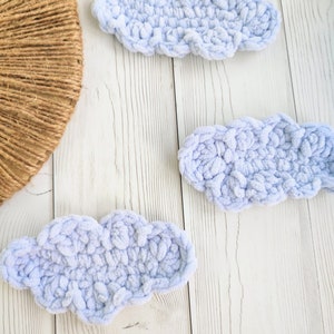 Puede incluir: Tres nubes de ganchillo de color azul claro sobre un fondo de madera blanco.