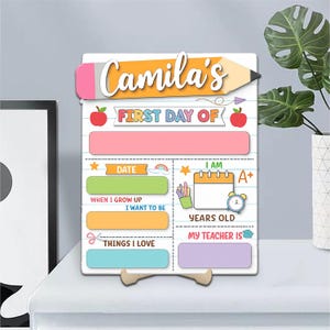 May include: A colourful wooden sign for the first day of school, personalised with "Camila's". It has sections for the date, age, teacher's name, and things loved, with graphics like apples and pencils. Measurements are in centimeters.