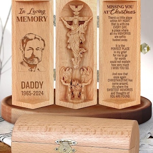 May include: A wooden box with a hinged lid, featuring a carved image of Jesus on the cross. The box is engraved with the words "In Loving Memory" and "Missing You at Christmas". The box also includes a small photo of a man and the text "Daddy 1965-2024".