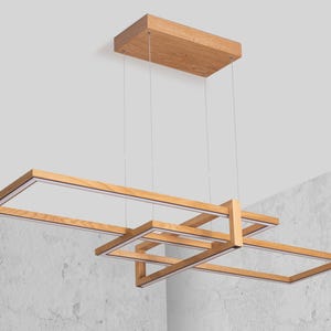 May include: A modern wooden chandelier with a geometric design. The chandelier has four rectangular frames made of natural wood, with LED lights inside each frame. The chandelier is suspended from the ceiling by four wires.